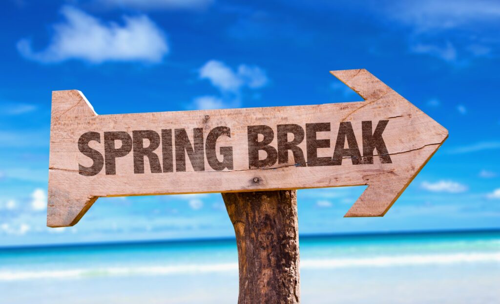 A wooden way sign etched with "SPRING BREAK" points the way, seaside, for stay healthy while traveling for spring break blog.