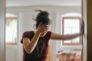 A woman suffering from vertigo or dizziness braces herself in a doorway, holding her head for "Should I Go to Urgent Care for Dizziness" blog.