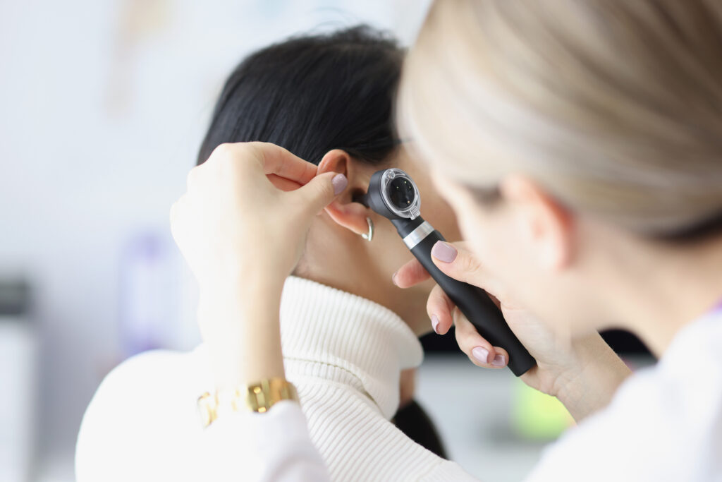 A doctor examines a female patient's ear with an otoscope for should-I-go-to-urgent-care-for-earwax-buildup blog.
