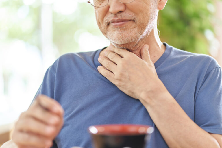 An older man places his hand to his throat for should-i-go-to-urgent-care-for-difficulty-swallowing blog.