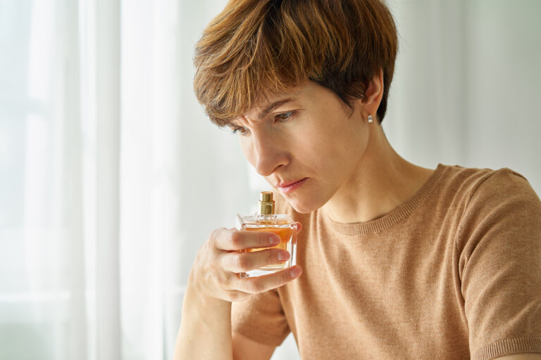 A Caucasian woman sniffs a perfume bottle for should-I-go-to-urgent-care-for-a-sudden-loss-of-smell blog.