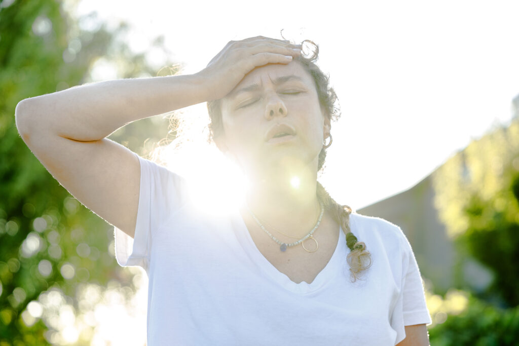 A young woman sweating on a hot summer day holds her head, fatigued, for urgent-care-for-heat-exhaustion blog.